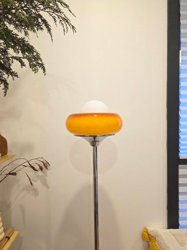 Retro modern Egg Tart Floor Lamp with chrome base with a yellow glass shade against a white wall.