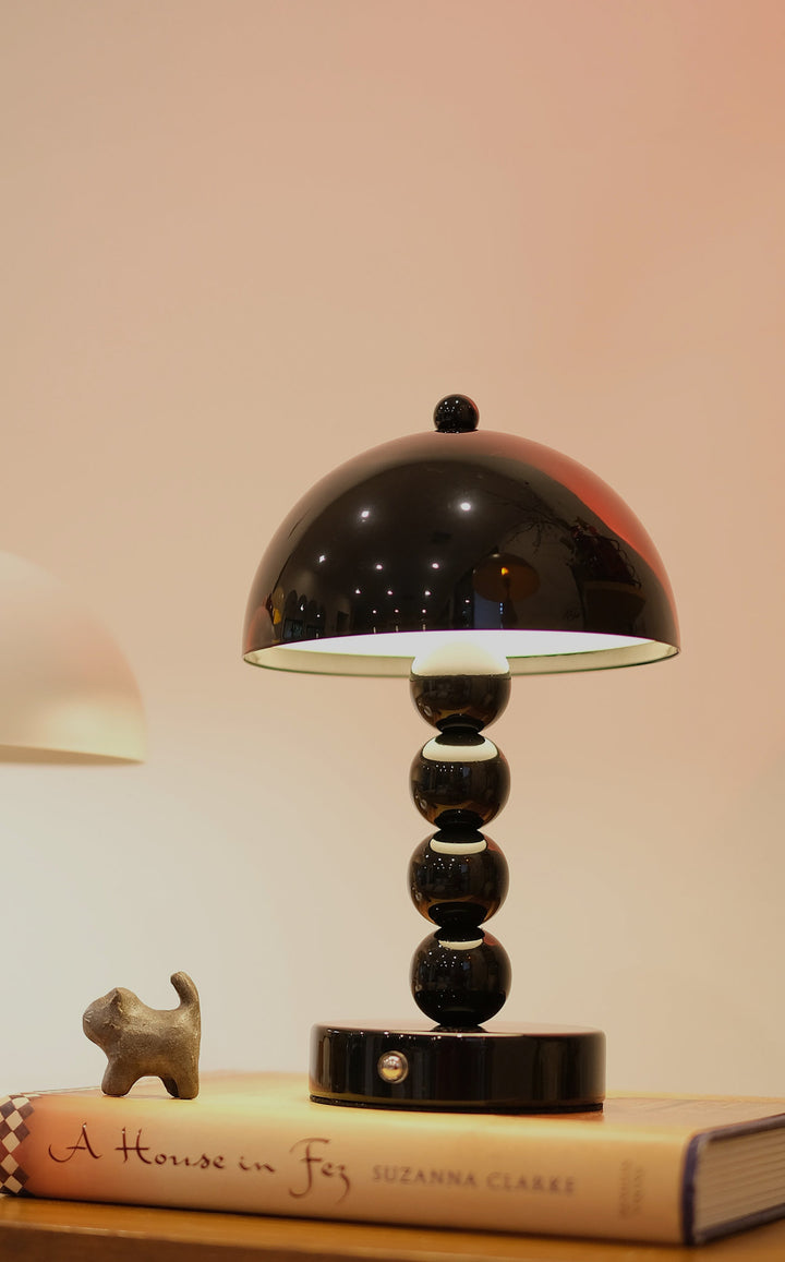 Black Bobbi Portable LED Table Lamp in white lacquer finish on bedside table on a book with a blurred background