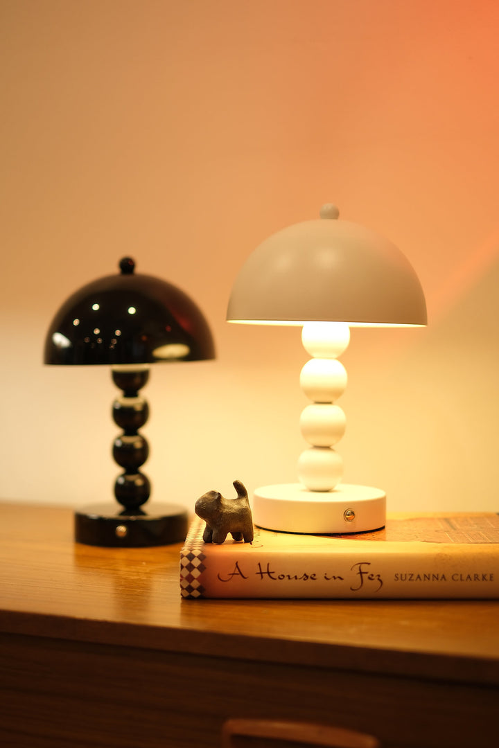 Two small Bobbi Portable LED Table Lamp in white lacquer finish on bedside tableon a surface with a book underneath, illuminated by the lamps.