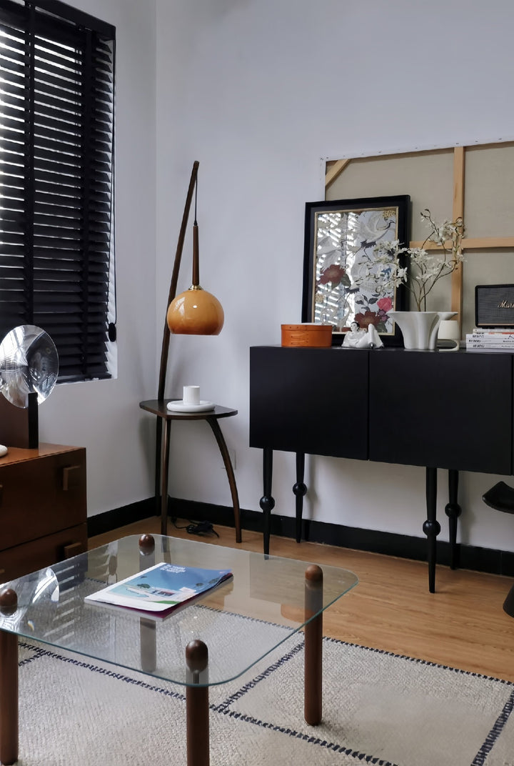 Living room with a black sideboard, glass coffee table, and decorative items. Retro floor lamp with glass shade and coffee table storage