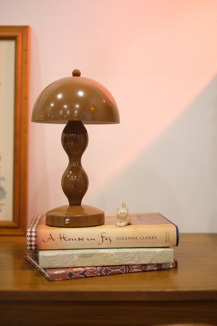 Retro mushroom lamp glowing softly in modern interior décor on a stack of books with a soft pink wall in the background