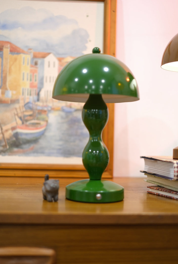 Dori LED lamp close-up showing touch switch base on a wooden surface with a painting in the background