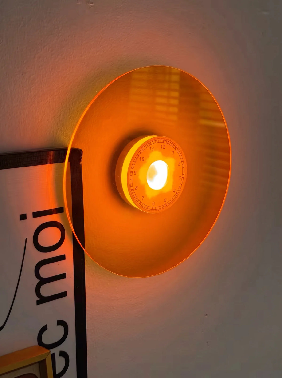 Wall-mounted retro lamp with round orange shield, amber light center, and black mounting arms