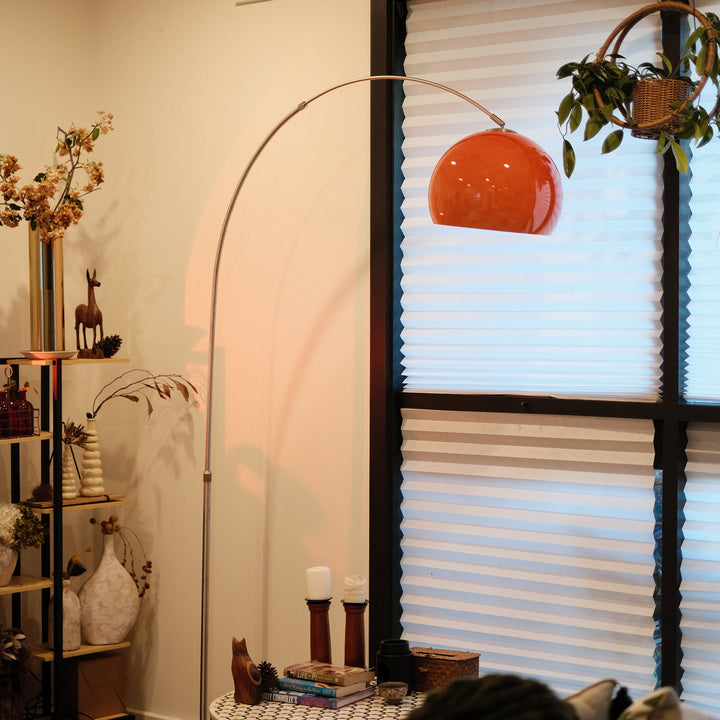 Sneedville+ Bauhaus Arc Floor Lamp with chrome arc and marble base in white shade Orange lamp casting a warm glow in a dimly lit room with posters and decor. Living room with a floor lamp, bookshelf, and window with blinds.