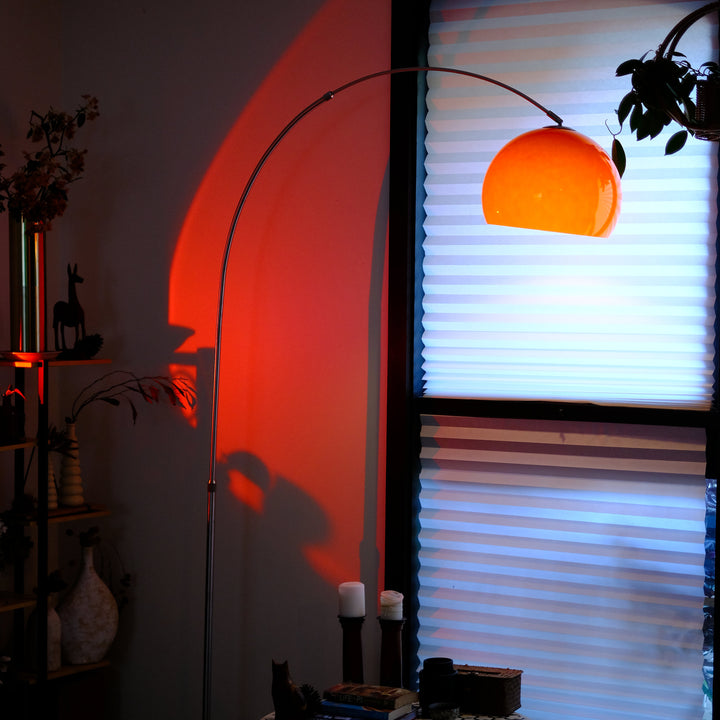 Sneedville+ Bauhaus Arc Floor Lamp with chrome arc and marble base in white shade Orange lamp casting a warm glow in a dimly lit room with posters and decor. Orange floor lamp casting a shadow on a wall with a window in the background
