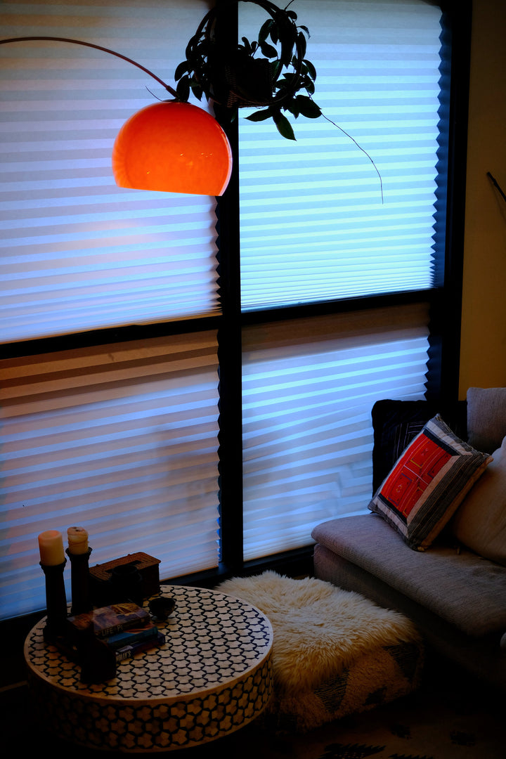 Sneedville+ Bauhaus Arc Floor Lamp with chrome arc and marble base in white shade Orange lamp casting a warm glow in a dimly lit room with posters and decor. Living room with a round table, sofa, and window blinds