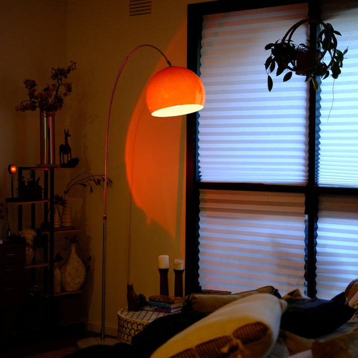 Sneedville+ Bauhaus Arc Floor Lamp with chrome arc and marble base in white shade Orange lamp casting a warm glow in a dimly lit room with posters and decor. Living room with a floor lamp casting an orange glow, a window with blinds, and decorative items.