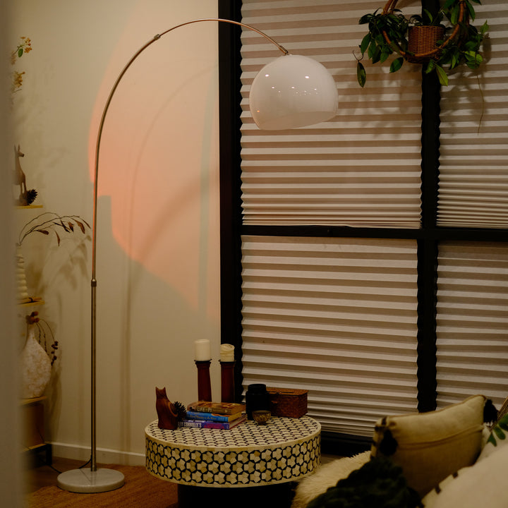 Sneedville+ Bauhaus Arc Floor Lamp with chrome arc and marble base in white shade casting a warm glow in a dimly lit room with posters and decor. Floor lamp with a white shade against a striped wall Living room with a floor lamp, small table, and decorative items.