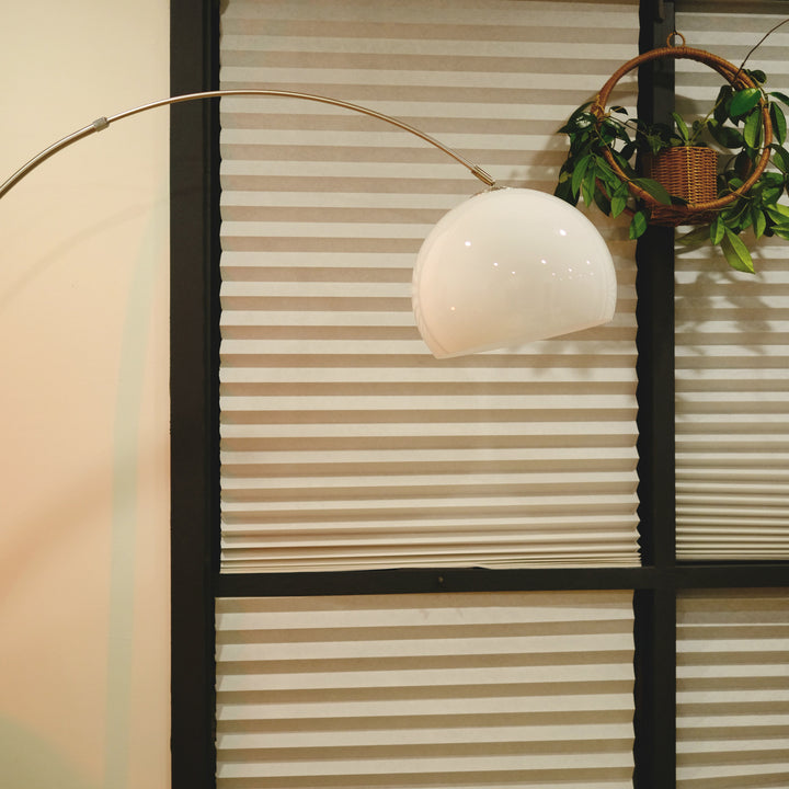 Sneedville+ Bauhaus Arc Floor Lamp with chrome arc and marble base in white shade casting a warm glow in a dimly lit room with posters and decor. Floor lamp with a white shade against a striped wall