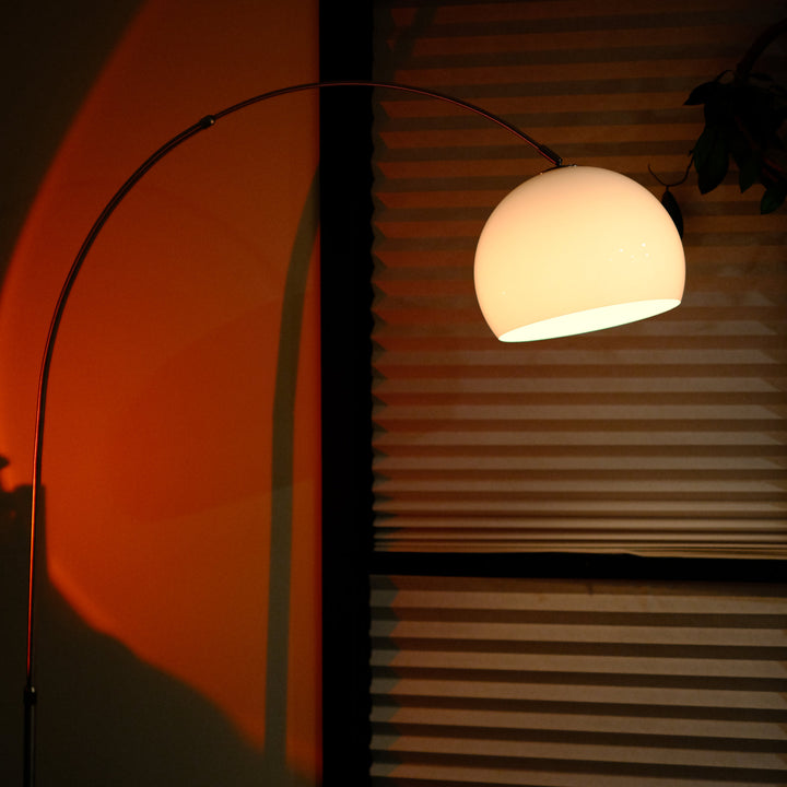 Sneedville+ Bauhaus Arc Floor Lamp with chrome arc and marble base in white shade casting a warm glow in a dimly lit room with posters and decor. Floor lamp with a white shade against a striped wall Floor lamp casting a shadow on a wall with a window in the background