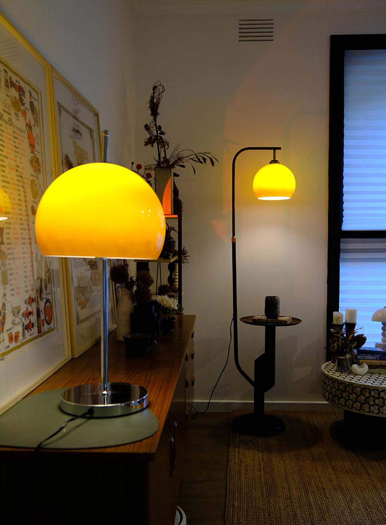 Two yellow lamps in a room with a shelf and window.